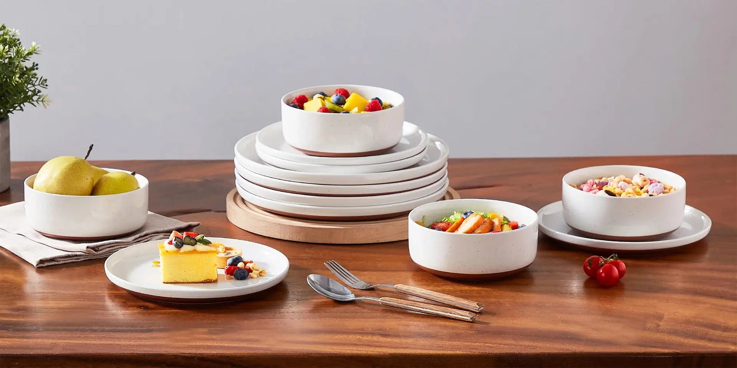 Elegant white dinnerware set on wooden table with fruit, salad, and dessert, showcasing modern minimalist design.