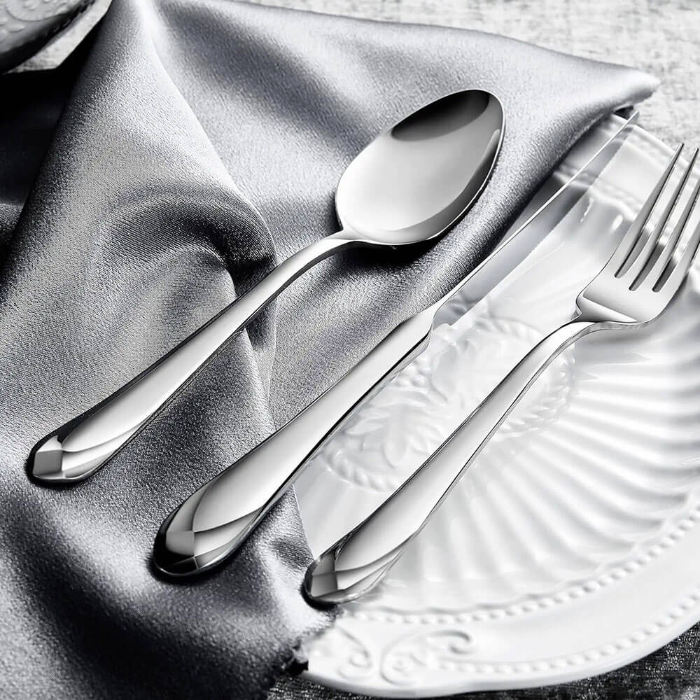 Elegant 18 10 stainless steel flatware with fork, knife, and spoon on white plate and silver fabric.