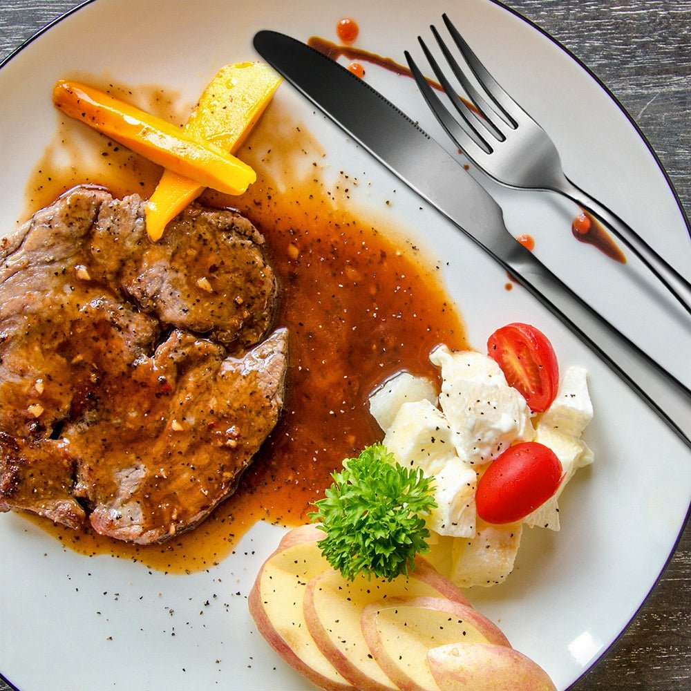Fork and knife on a dinner plate with steak, gravy, bell pepper, salad, apple slices, and parsley garnish.