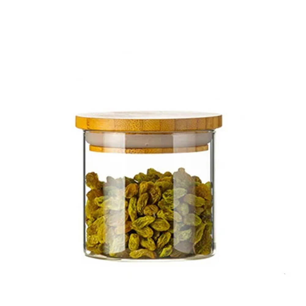 A clear cylindrical bamboo and glass jar filled with green raisins, featuring a flat natural bamboo lid with a silicone gasket for an airtight seal.