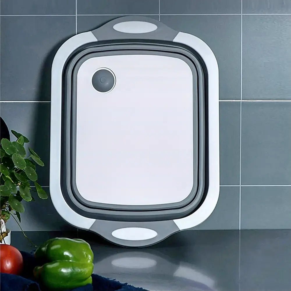 Gray and white BBQ collapsible cutting board shown standing upright on a kitchen counter, with vegetables placed nearby.