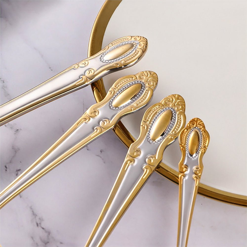 Close-up of ornate flatware handles with gold detailing, placed beside a white plate with a gold rim on a marble surface.