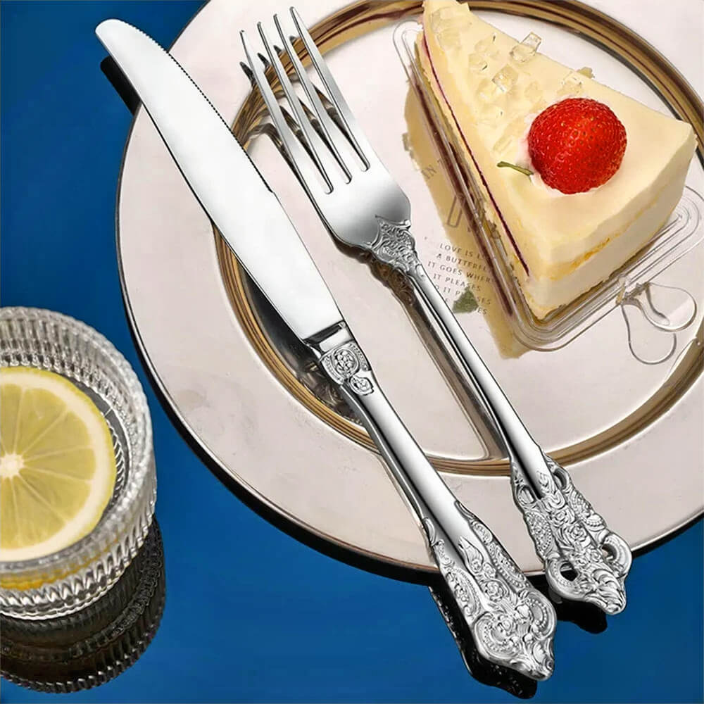 best stainless steel flatware sets with ornate knife and fork placed on plate with cake slice and lemon drink on blue surface.