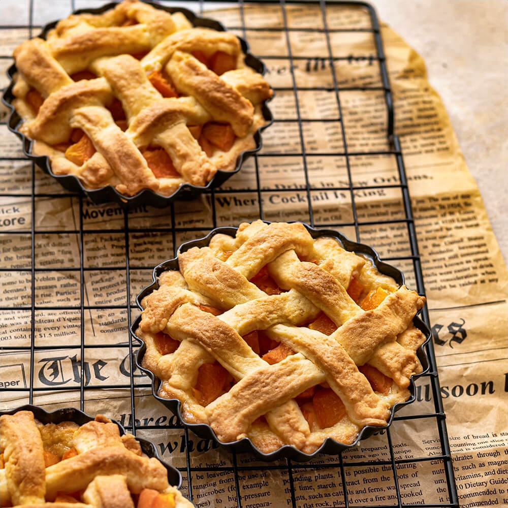 Mini lattice-crust fruit pies in the best tart pan with removable bottom on a cooling rack, with golden-brown crusts and a warm fruit filling.