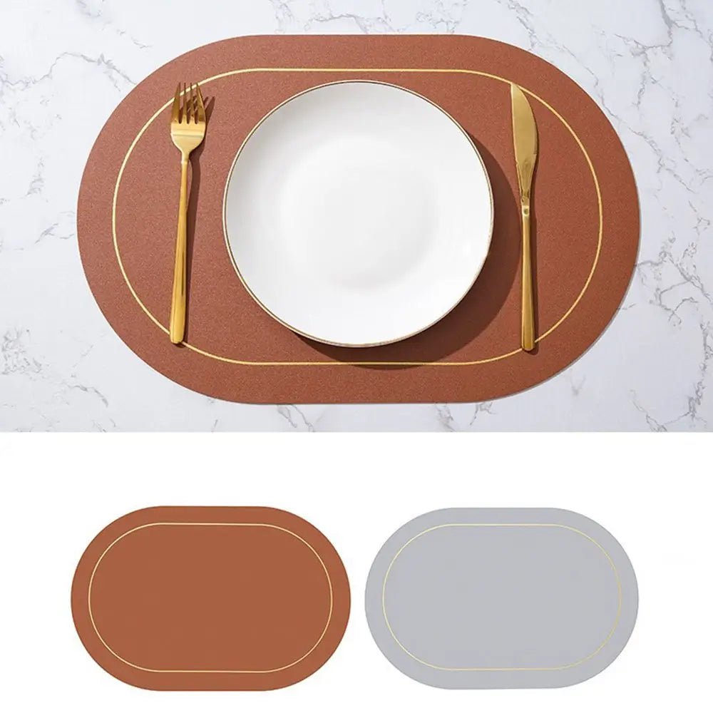 Brown faux leather placemats with gold trim, reversible to light gray, displayed on a marble table with a white plate and gold cutlery.