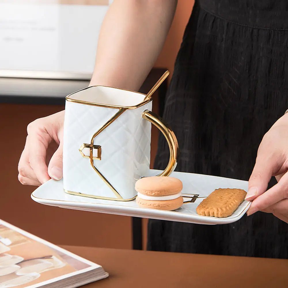 Person holding a tray with coffee mug handbag design in white and gold, served with a biscuit and a macaron.