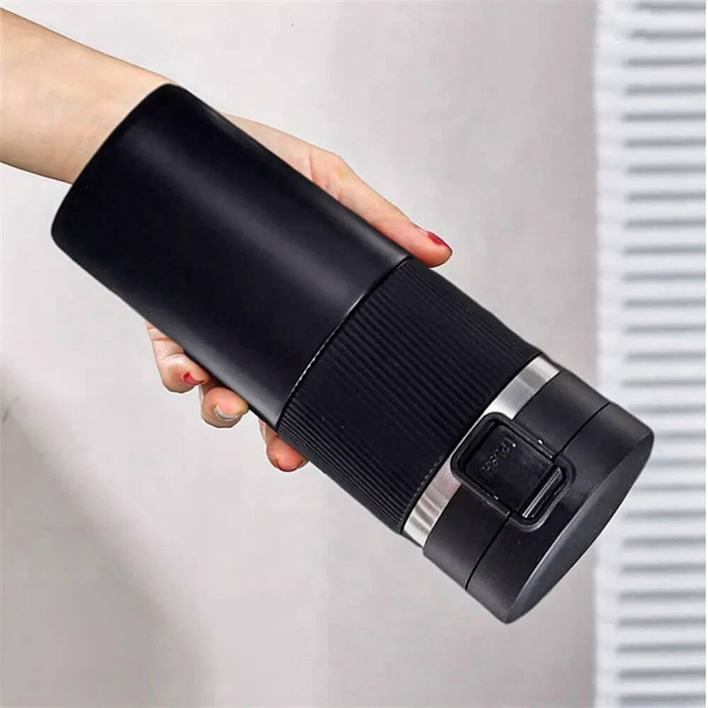 Hand holding a black coffee tumbler stainless steel with a textured grip, one-click locking lid, and a sleek matte finish, shown against a neutral background.