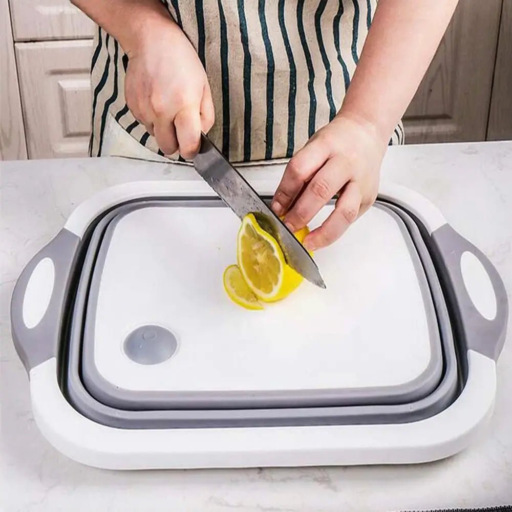 Person slicing a lemon on a gray and white collapsible cutting board with colander, used flat as a stable chopping surface.