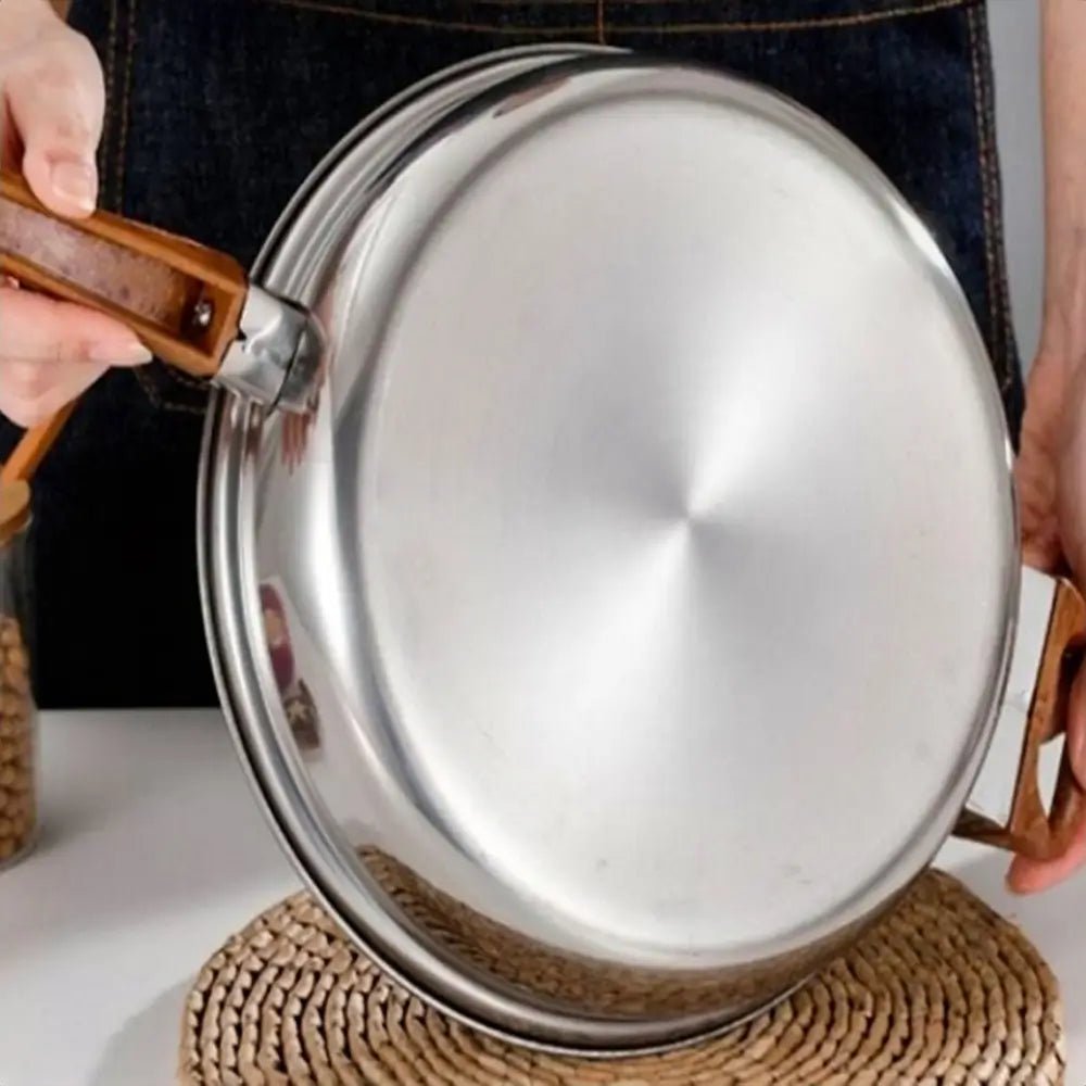 Cookware sets stainless steel frying pan with wooden handles held over a woven mat, showing the base of the pan.