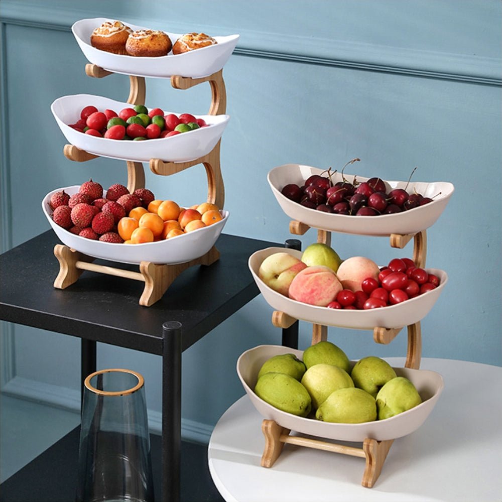 Decorative fruit bowl on two tiered wooden stands with curved ceramic bowls filled with cherries, lychees, peaches, and muffins.