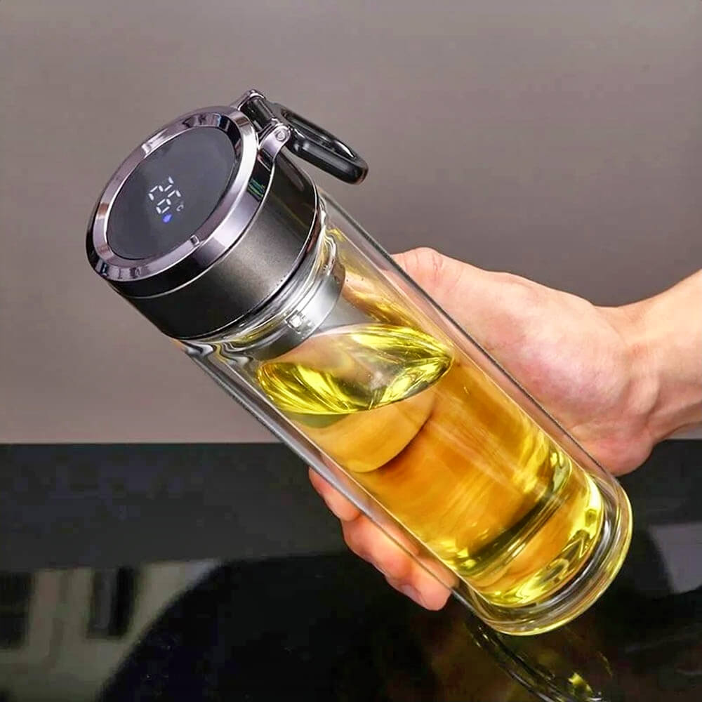A person holding a double-walled glass travel tumbler filled with a yellow liquid. The tumbler features a modern lid with a digital temperature display and a black carabiner clip for portability, showcasing its sleek and functional design.