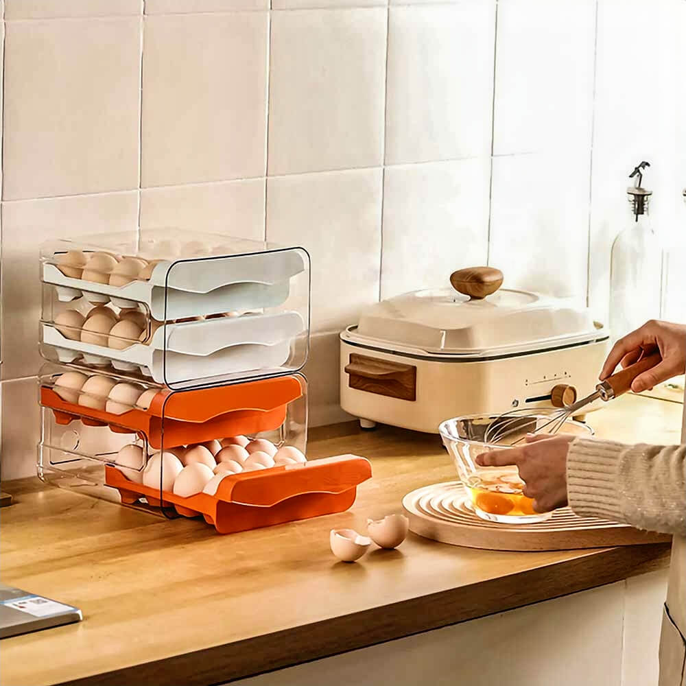 Person whisking eggs beside stacked egg storage containers with white and orange drawers on kitchen counter near broken eggshells.