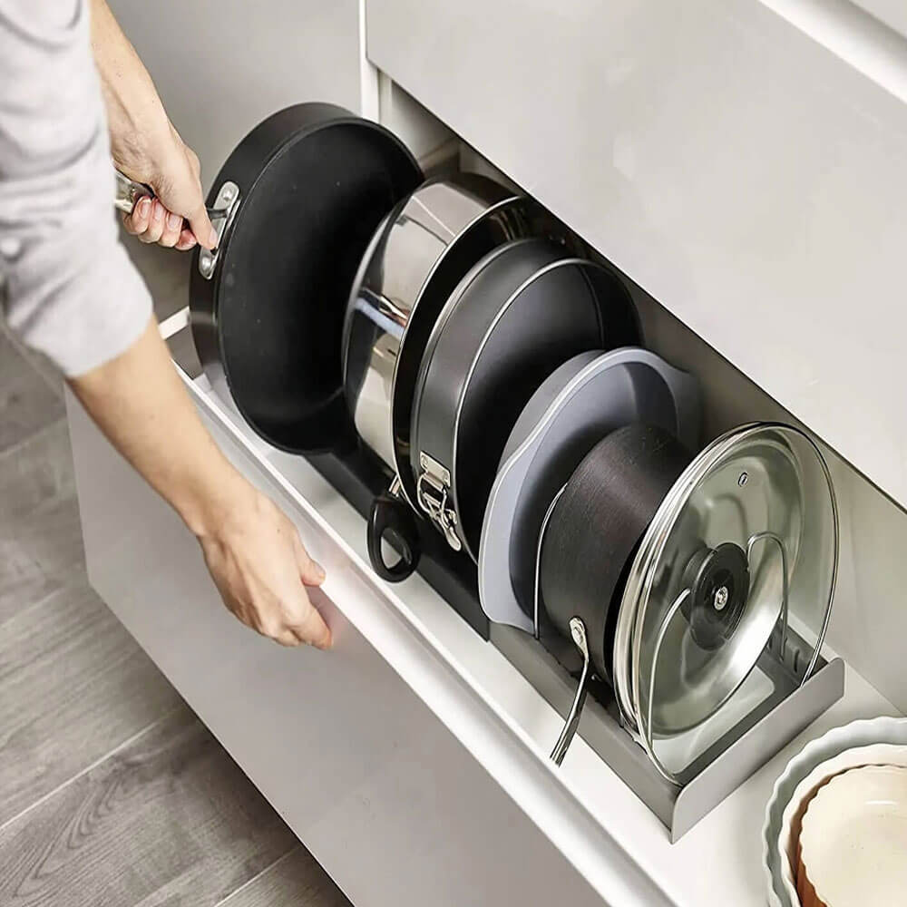 An efficient expandable pans organizer rack neatly holds a variety of cookware, including pans, pots, and lids, inside a kitchen drawer. A hand is seen reaching for a pan, showcasing the organizer&