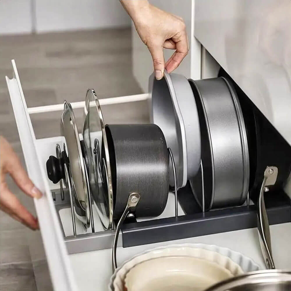 An organized expandable pot rack securely holds pots, pans, and lids in a drawer. Hands are seen adjusting cookware, demonstrating the rack&