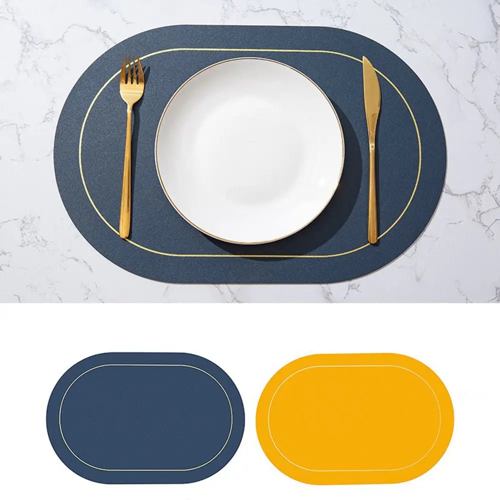 Faux leather placemat in navy blue with gold trim, reversible to mustard yellow, displayed on a marble table with a white plate and gold cutlery.