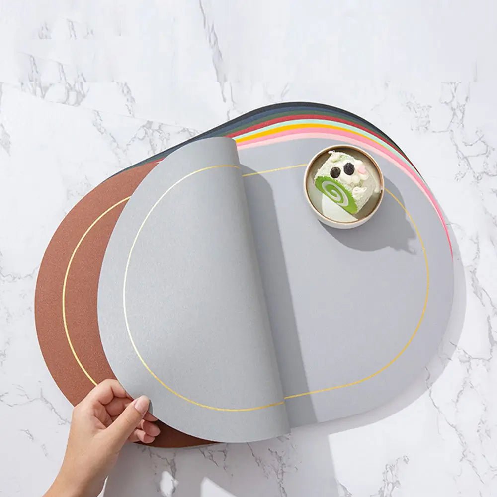 Faux leather placemats in assorted colors, shown stacked with a hand lifting the top gray mat, placed on a marble table with a dessert plate.