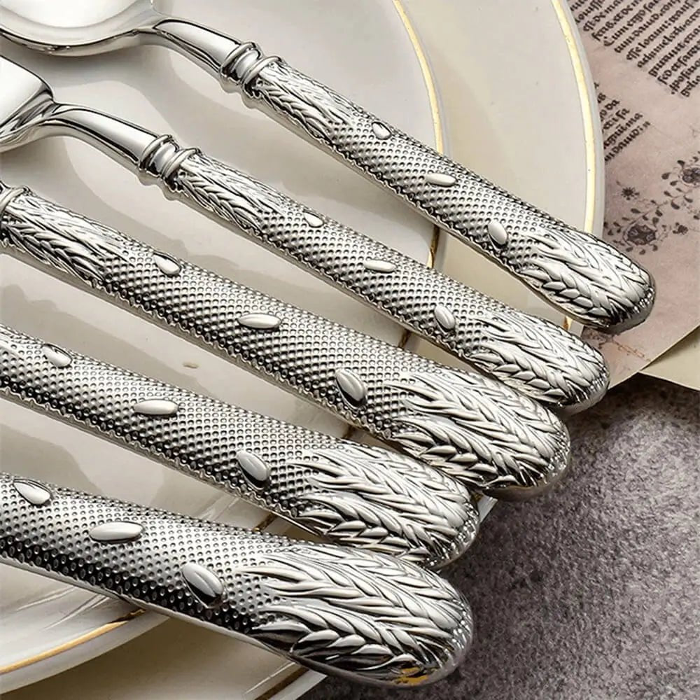 Flatware collections with textured silver handles featuring wheat details, placed over white plates on a soft textured surface.