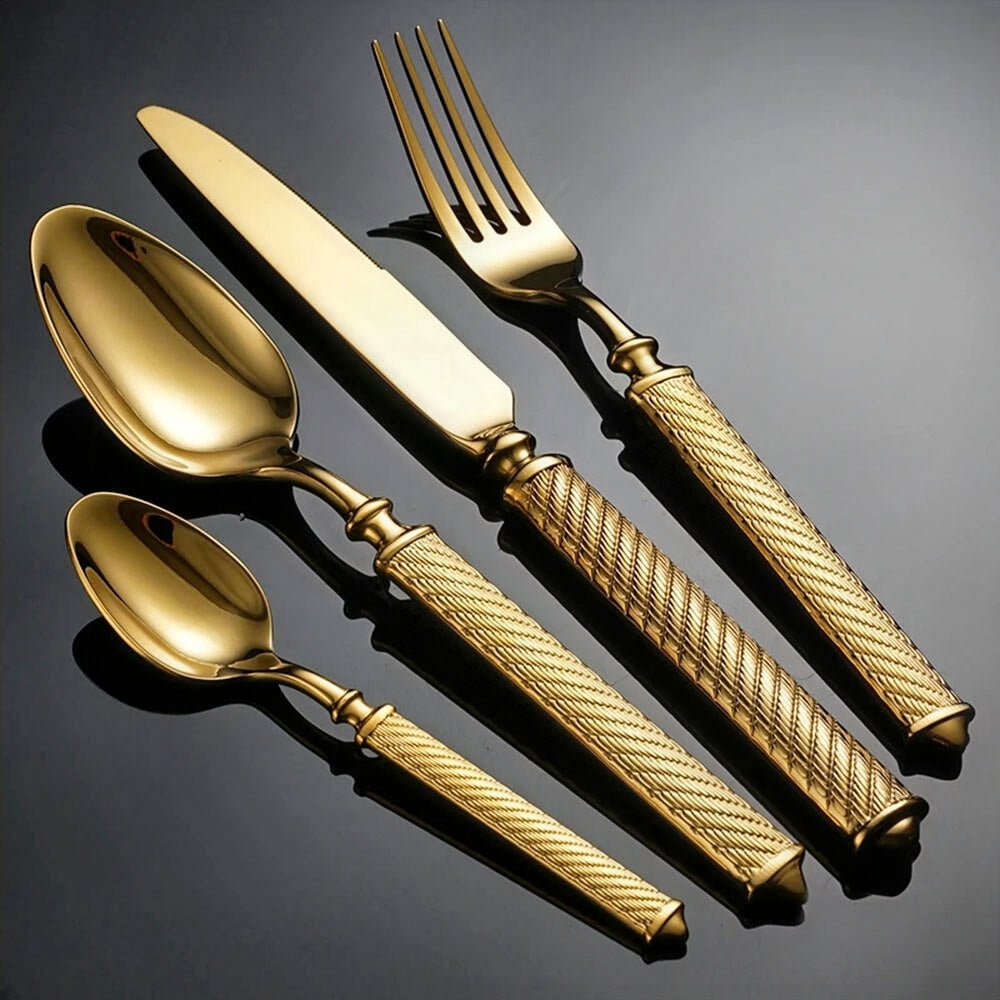 A gold flatware cutlery set featuring a knife, fork, tablespoon, and teaspoon. Each piece has a polished, reflective surface with textured handles. The set is displayed on a dark background, emphasizing its luxurious and elegant design.