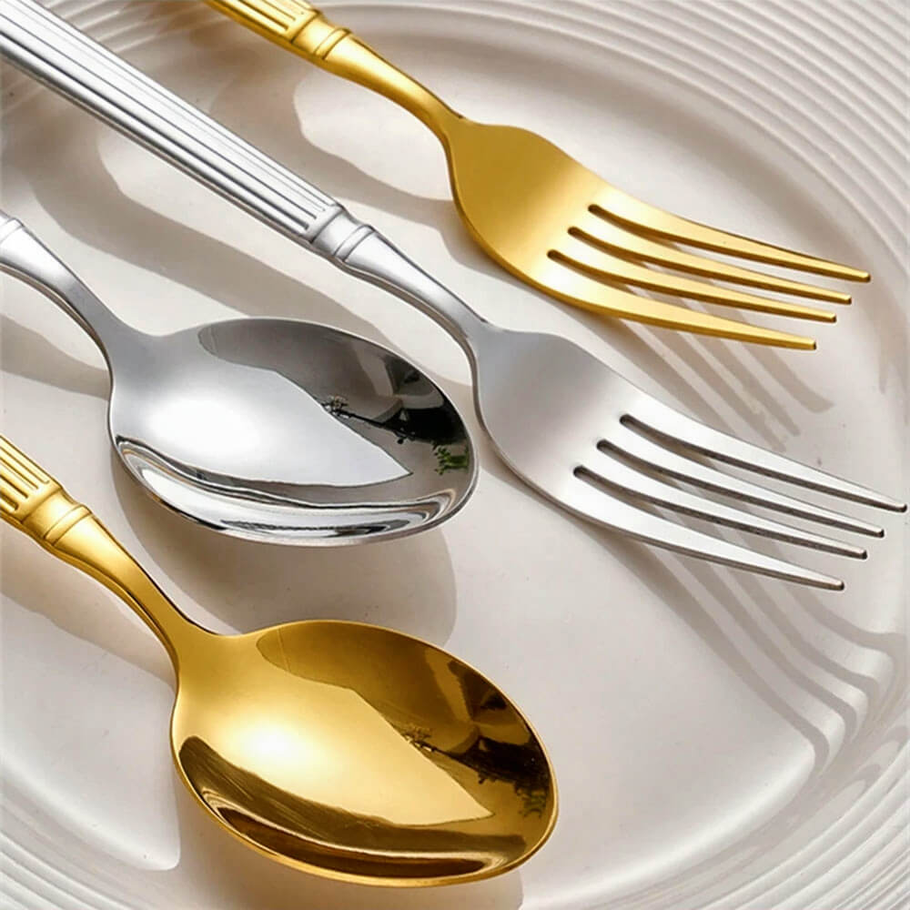 Close-up of modern gold and silver flatware featuring a fork and spoon in each finish, displayed elegantly on a white ridged plate.