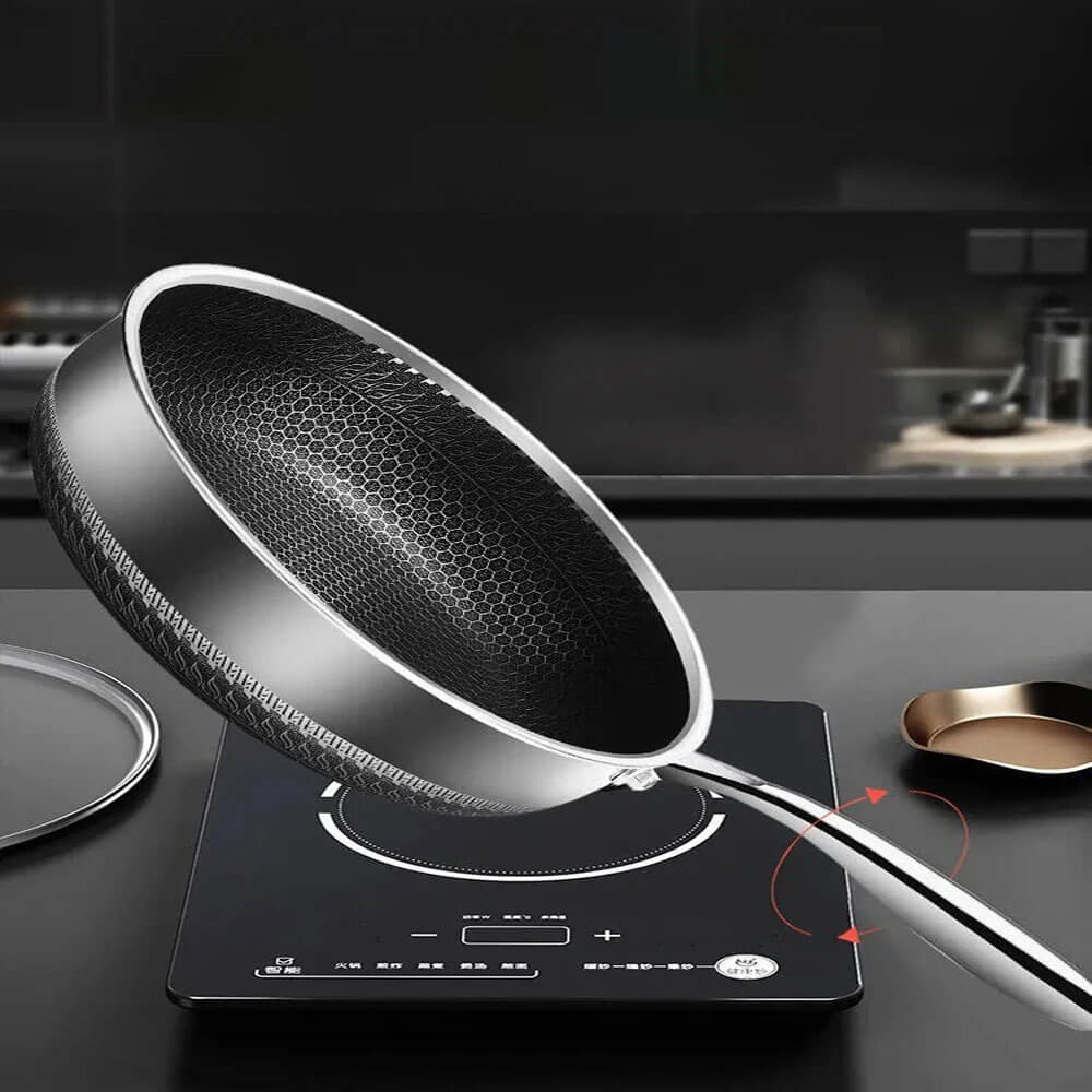 Frying pan honeycomb design with non-stick surface and curved handle, shown tilted over a black stovetop in modern kitchen.