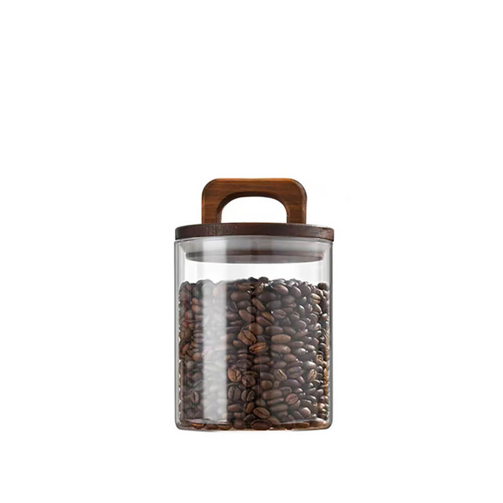 A transparent glass pantry storage jar filled with coffee beans, featuring a dark wooden lid with a built-in handle, set against a plain white background.