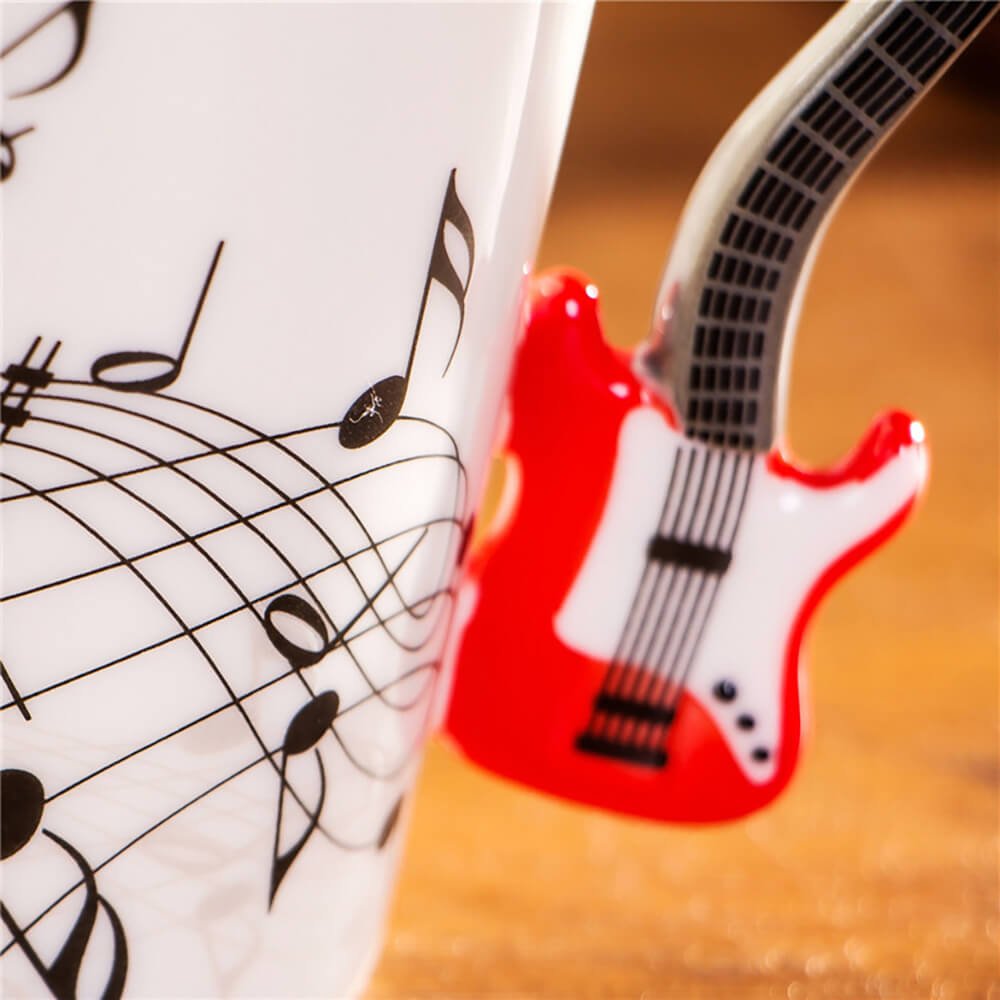 Close-up of a white guitar handle coffee mug with black music notes and a red electric guitar-shaped handle.