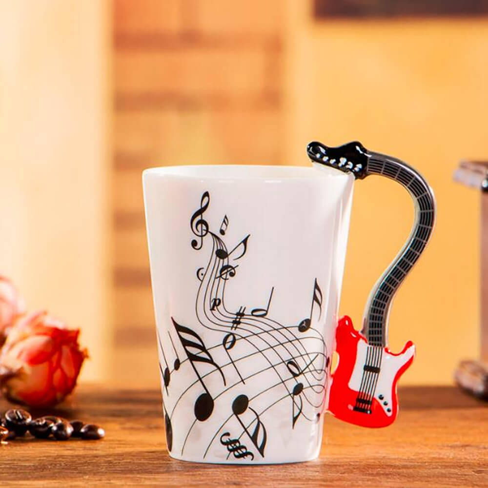 White ceramic electric guitar mug with music notes and a red guitar-shaped handle placed on a wooden surface.