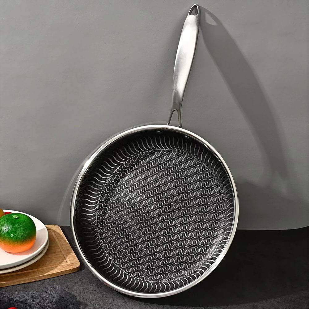 Stainless steel honeycomb frying pan with textured nonstick surface, long handle, and a modern setup beside plates and fruits.
