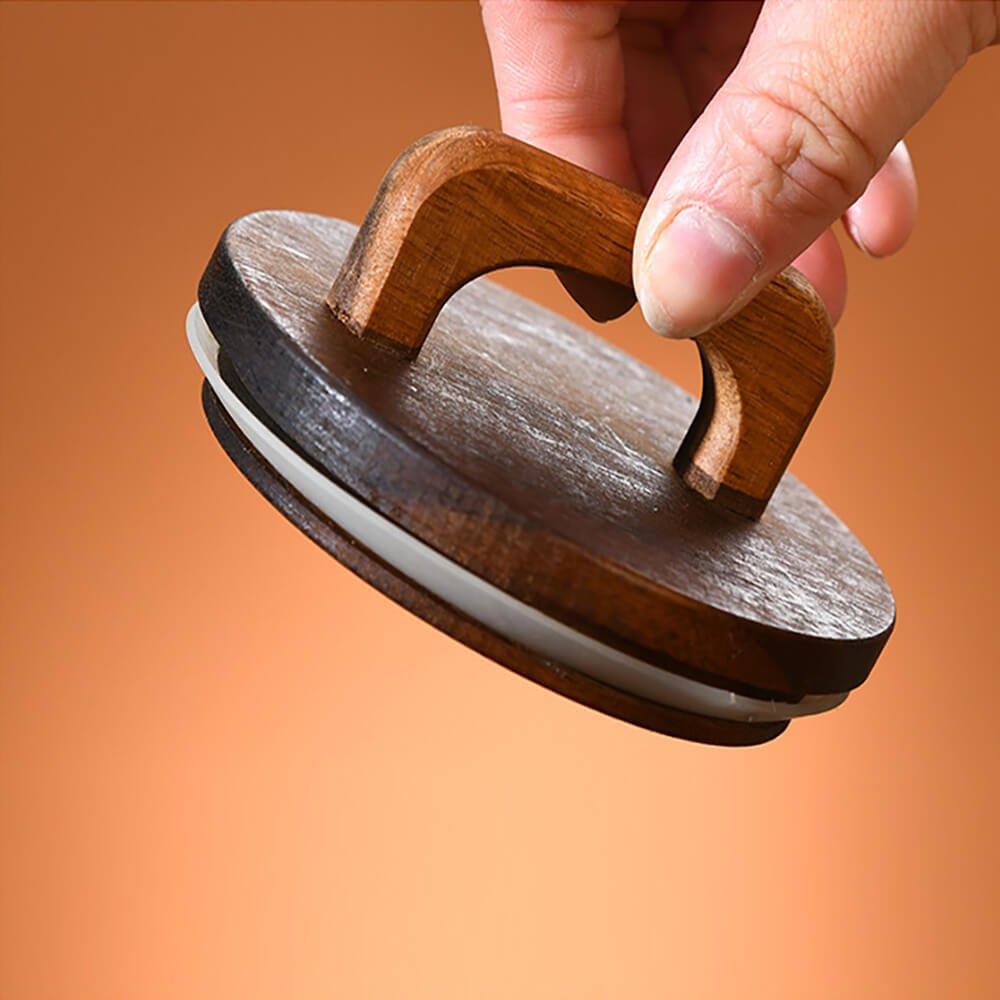 A close-up image of a wooden jar lid with a built-in handle, held by a person&