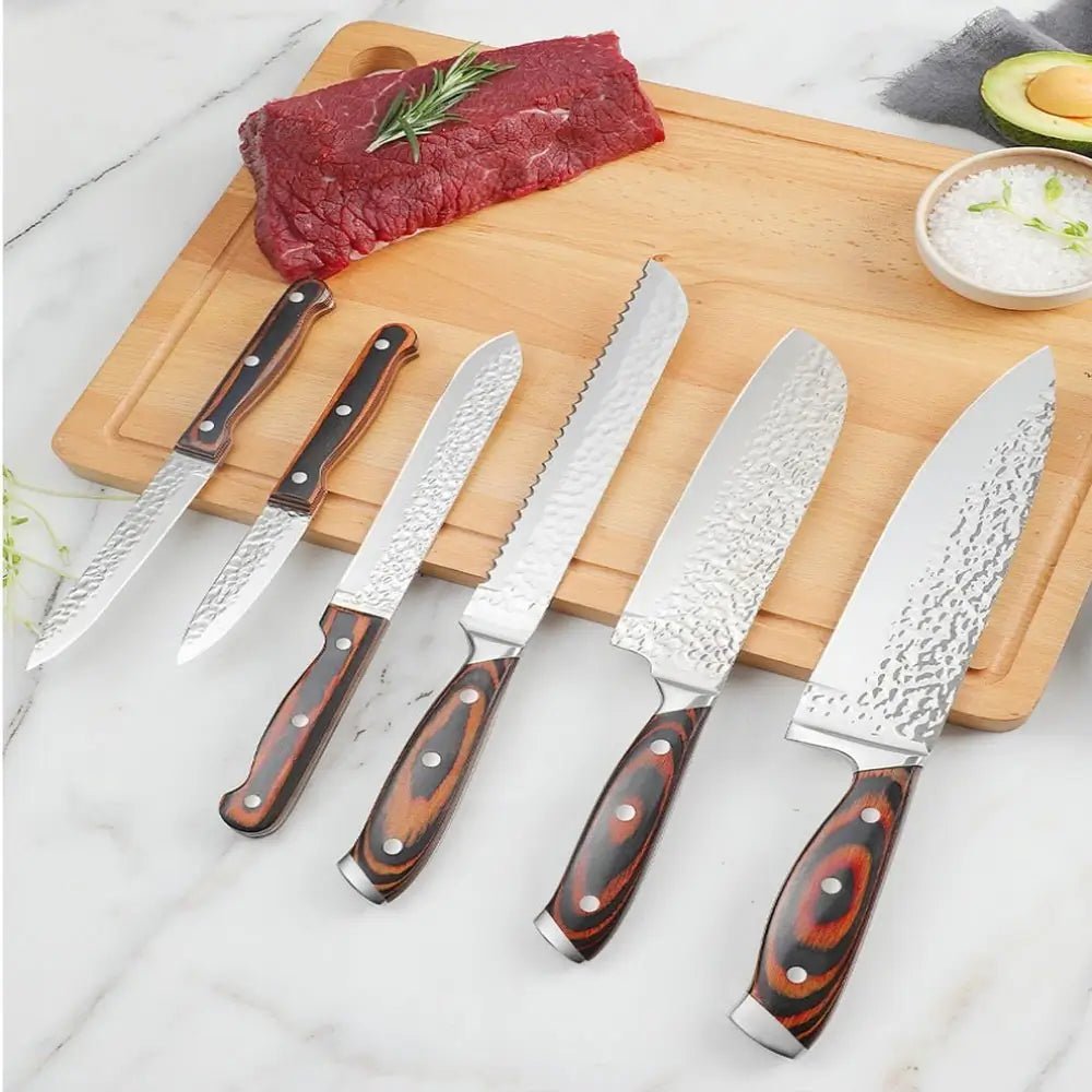 Knife set and block with hammered stainless steel blades and wooden handles, displayed on cutting board with raw beef, avocado, and salt.