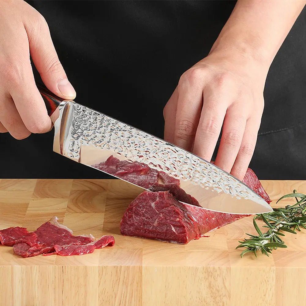 Close up of chef using hammered stainless steel knife from knife set with block to slice raw beef on wooden cutting board.
