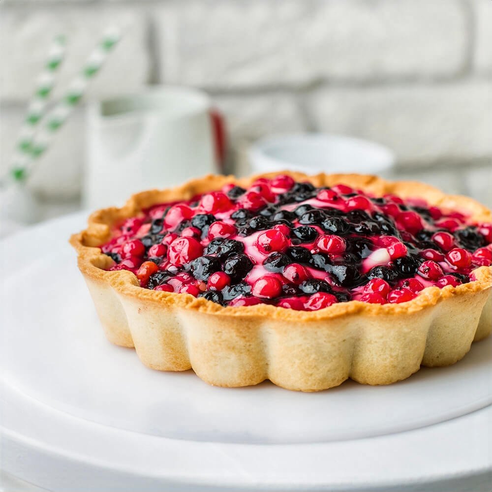 Mini tart filled with glossy red and black berries on a creamy base, served in a fluted crust made with a removable-bottom tart pan.