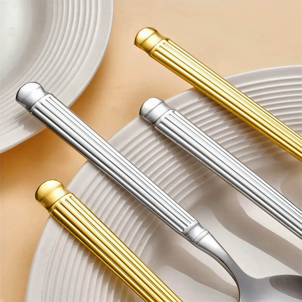 Close-up of gold and silver flatware handles with ridged texture, placed diagonally on white ceramic plates.