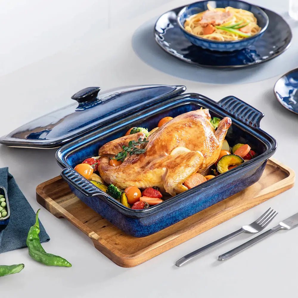 Blue porcelain casserole dish filled with roasted chicken and vegetables, placed on a wooden board with its matching lid beside it.
