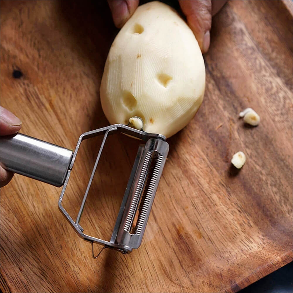 Stainless steel potato peeler removing potato eyes on a wooden cutting board, demonstrating its precision and efficiency in food preparation.