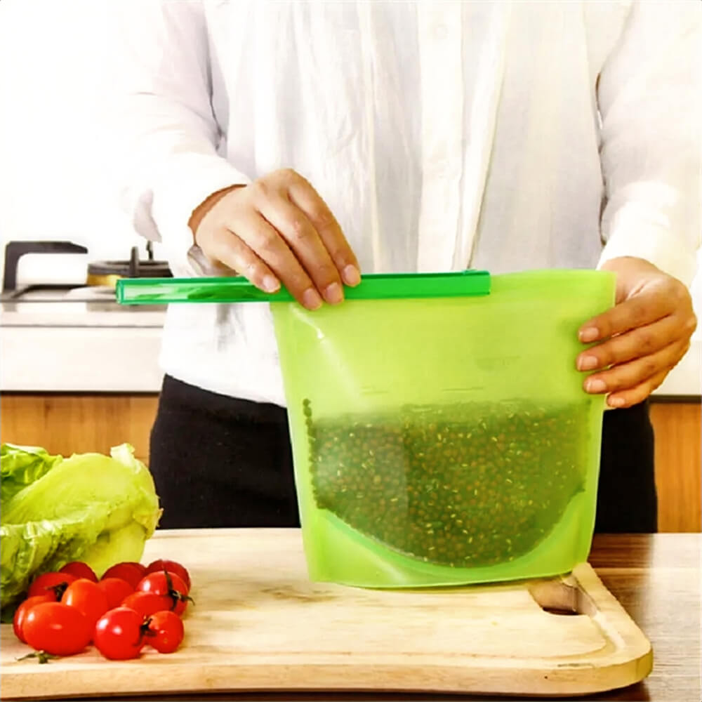 A person sealing a green reusable silicone bag filled with lentils, placed on a wooden cutting board with fresh vegetables.