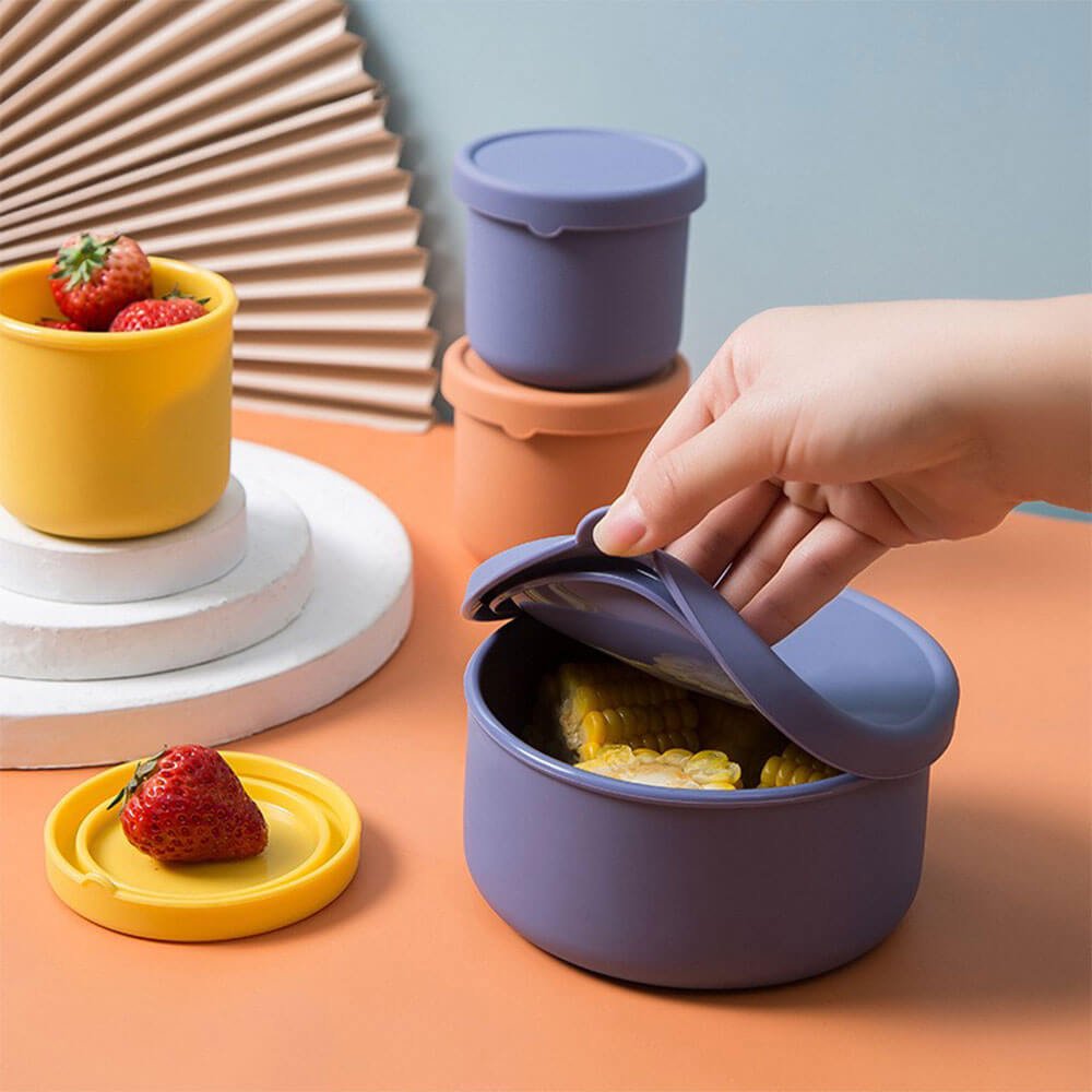 Colorful silicone containers for food in use, storing strawberries and corn; reusable, leakproof, and ideal for everyday meals.