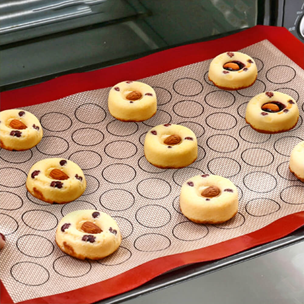 Silicone macaron baking mat with circular guides, featuring small baked donuts with almonds and raisins, placed inside an oven.