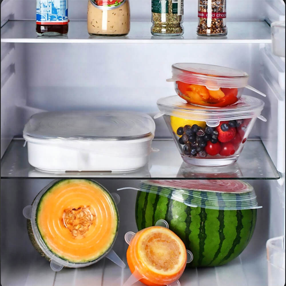Various fruits and bowls sealed with transparent silicone stretch lids inside a refrigerator, showing reusable food storage in Canada.