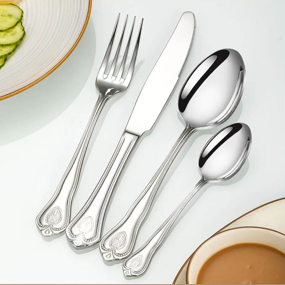 Shiny silver flatware set with ornate handles, placed beside a plate of sliced cucumbers and a cup of coffee.
