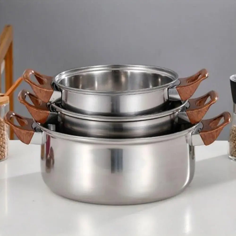 Stainless steel cookware set with three stackable pots featuring wooden handles displayed on a modern kitchen counter.