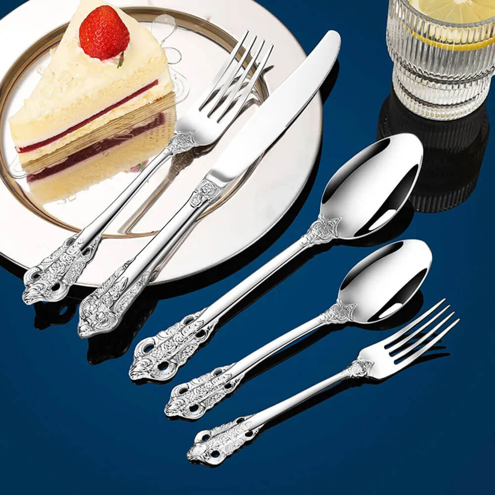 stainless steel flatware cutlery set with knife, forks, and spoons placed beside cake slice and lemon drink on dark background.