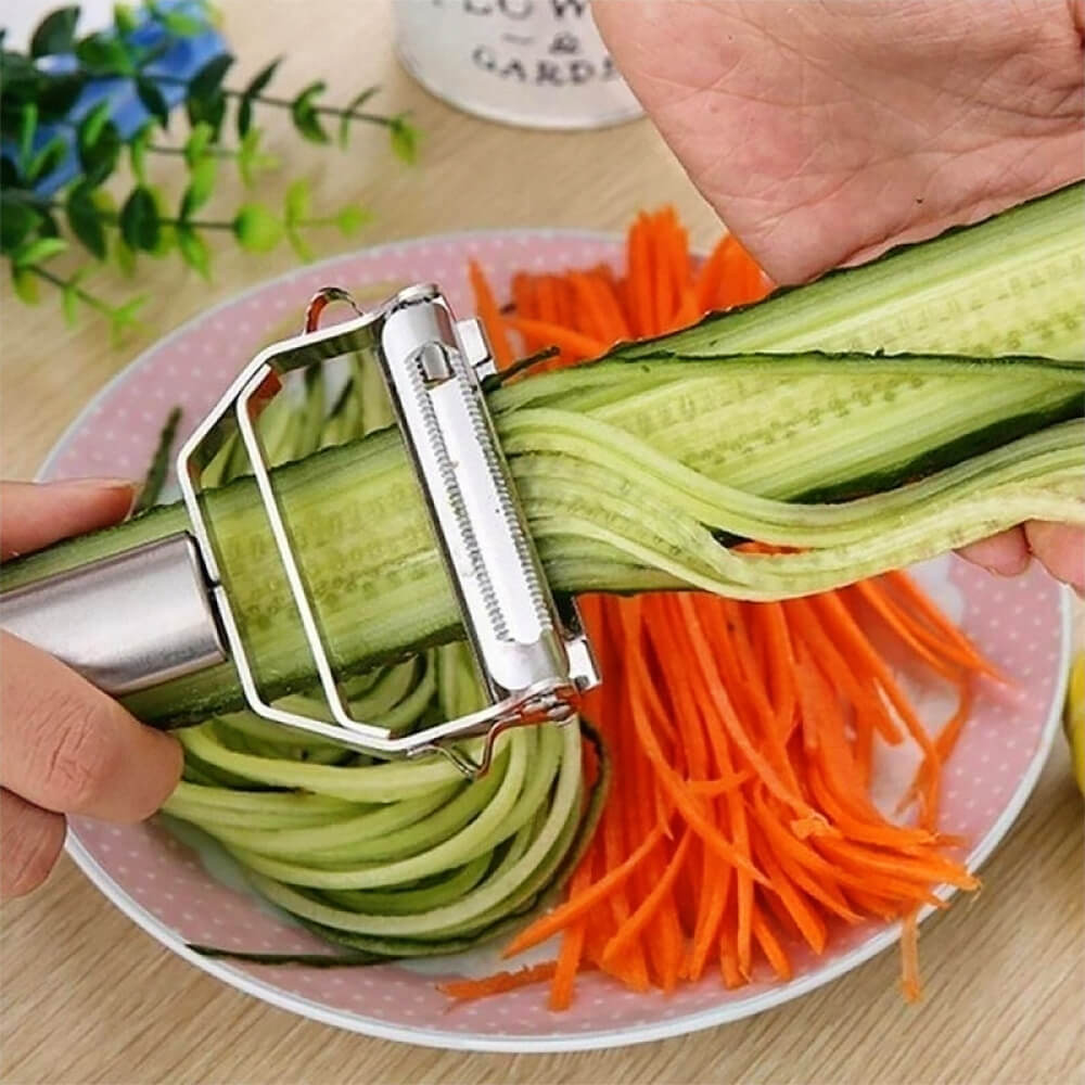 Stainless steel fruit and vegetable peeler in action, julienning cucumber into thin strips alongside shredded carrots. Ideal for multi-functional kitchen use.