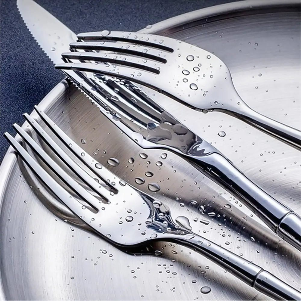 Elegant stainless steel silverware set with silver and gold pieces featuring bamboo-style handles, displayed on a dark background.