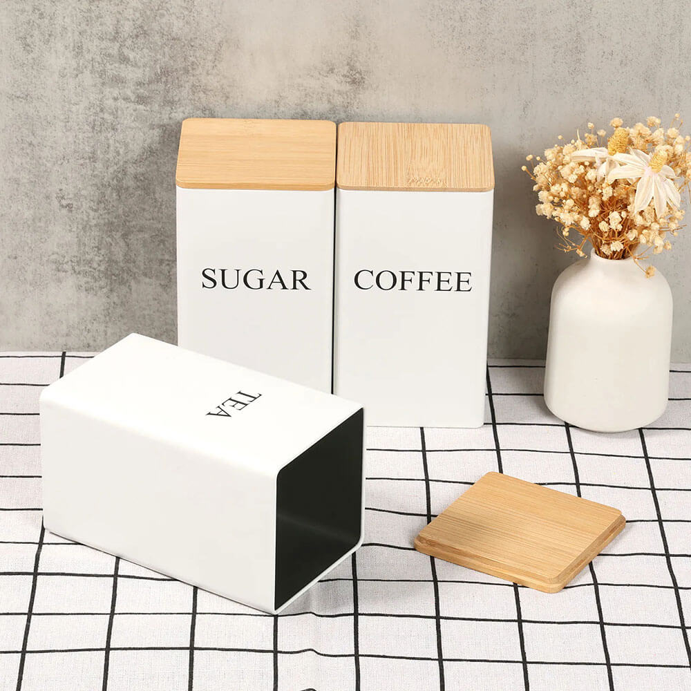 Three stainless steel storage containers for food labeled SUGAR, COFFEE, and TEA with bamboo lids, one container lying open.
