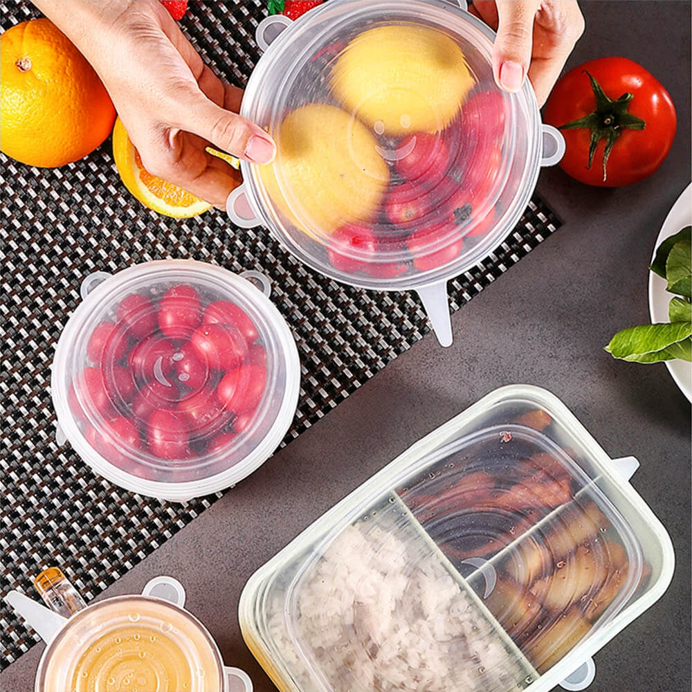Containers of fruits, drinks, and meals sealed with stretch-and-seal silicone lids on a kitchen counter with fresh produce nearby.