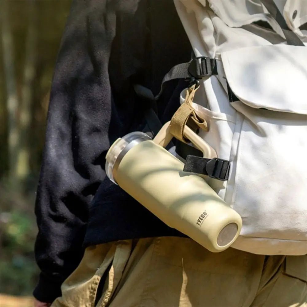 Beige TYESO thermal travel mug with lid attached to a backpack strap outdoors.