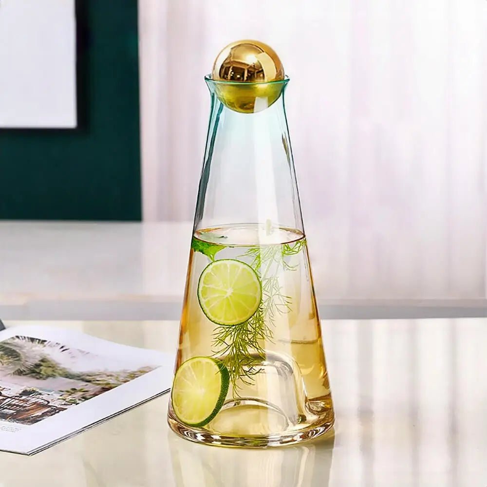 Glass water carafe and glass filled with citrus and herbs, placed on a table beside a magazine with soft natural light in the background.