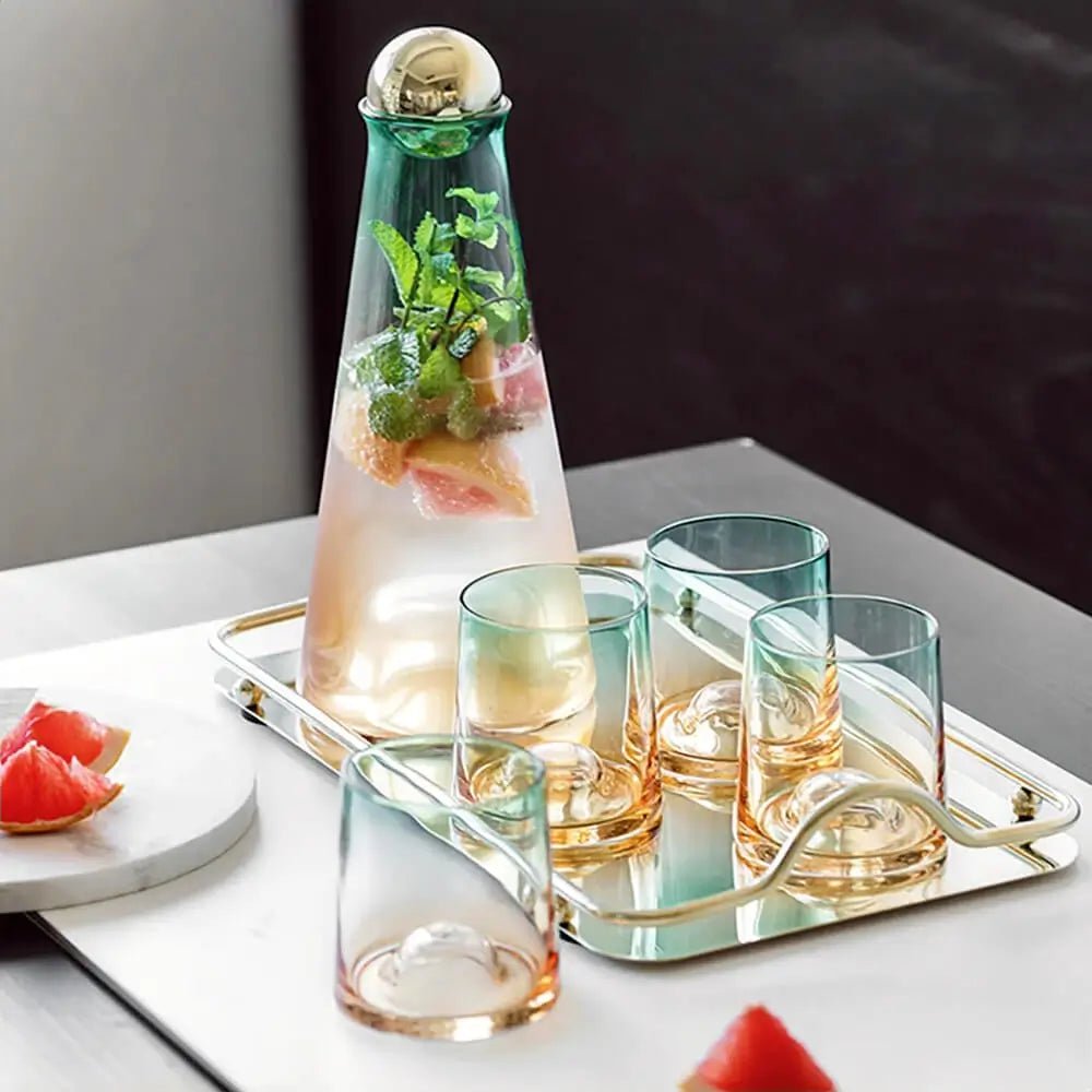 Glass water carafe and glass set with a gold tray, featuring a carafe filled with infused water and five gradient green and amber glasses.