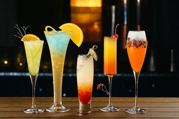 Colorful cocktails displayed in elegant drinking glassware, featuring various styles and garnishes on a wooden surface with a dark backdrop.